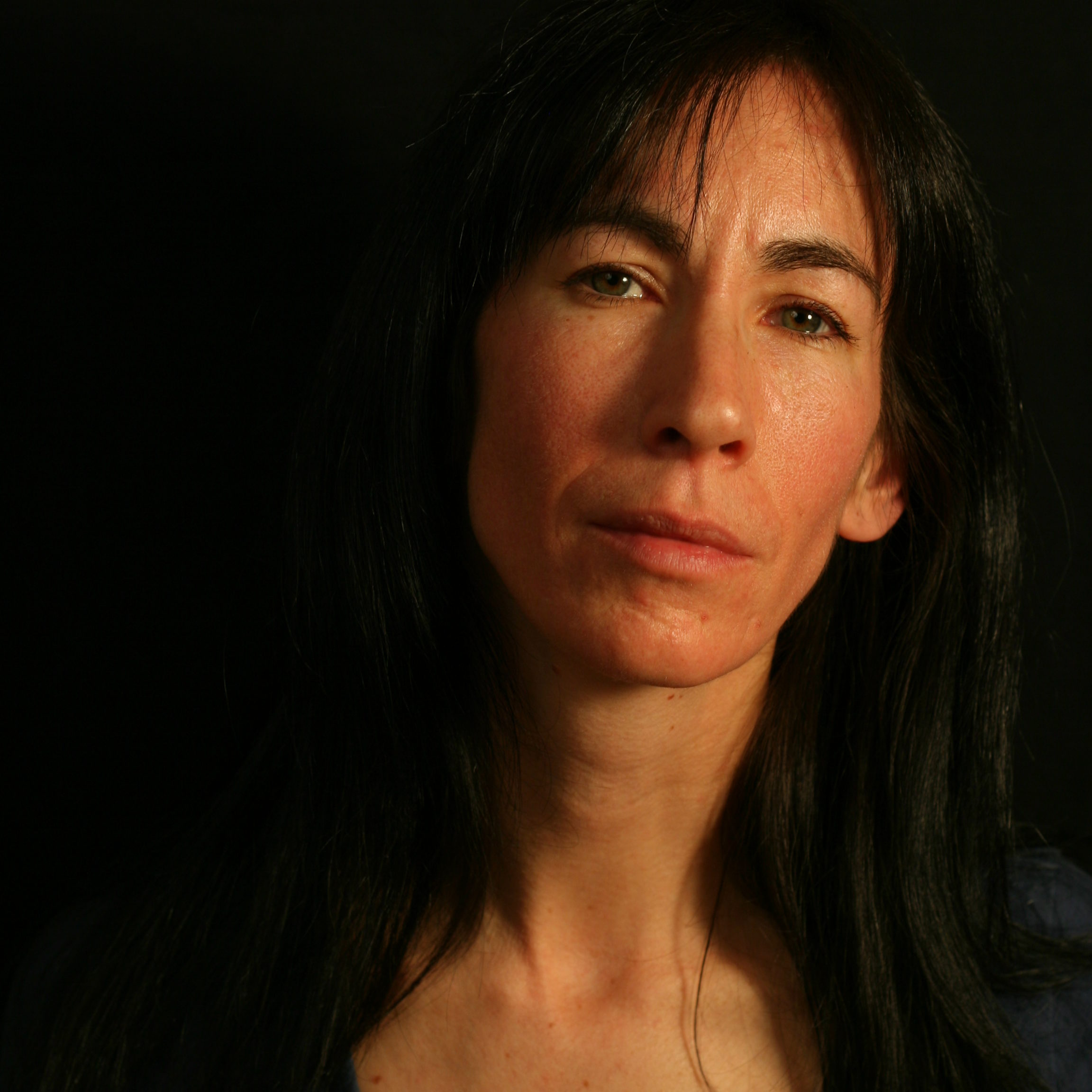 Photo portrait of a woman with dark hair in front on a dark background.